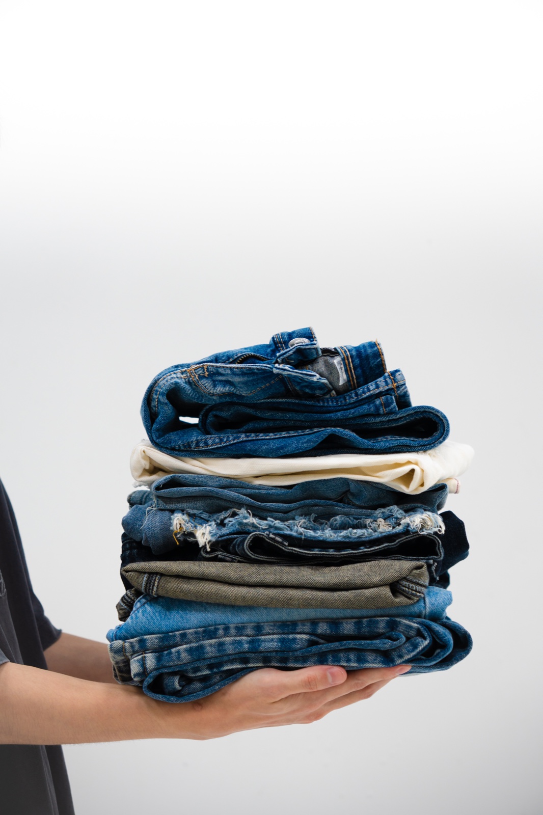 A hand holding a stack of donated denim garments